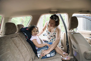 Mother securing daughter in booster seat