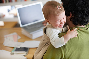 Parent emailing with doctor with crying baby on shoulder