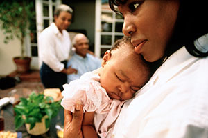 Mom holding sleeping baby while parents watch from background