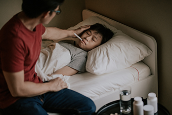 Young boy sick in bed with father taking his temperature