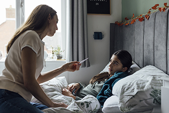 Teen girl in bed, mom checking her temperature